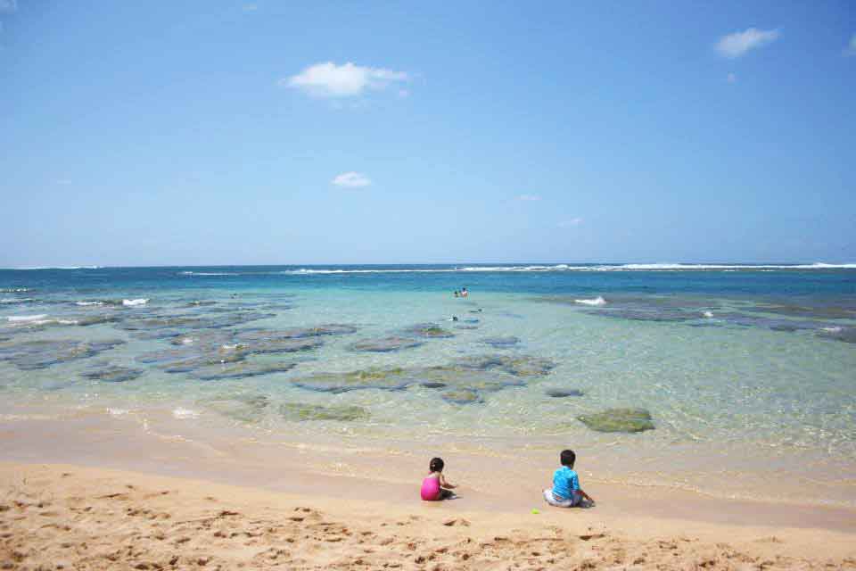 Golden sand beach with two children playing at water's edge of one of the most beautiful beaches in the world.